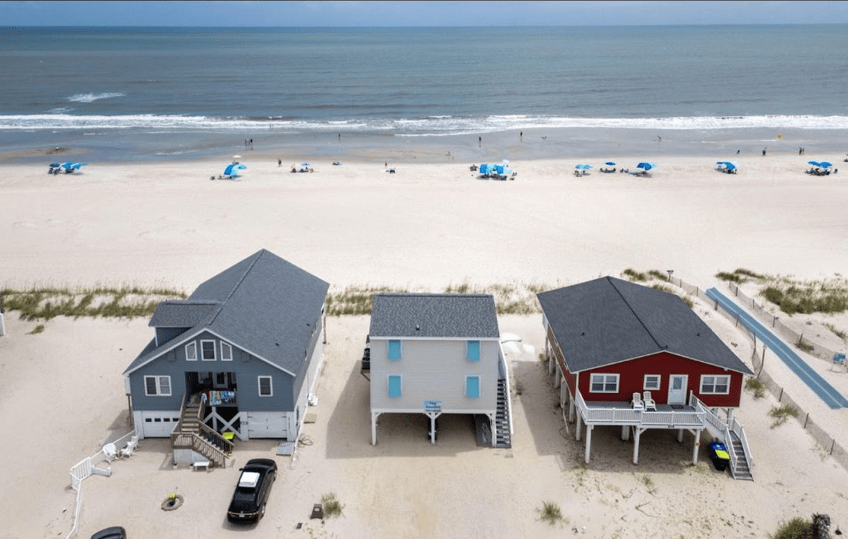 Aerial view of three beach houses, gray, white, and red, on sandy beachfront