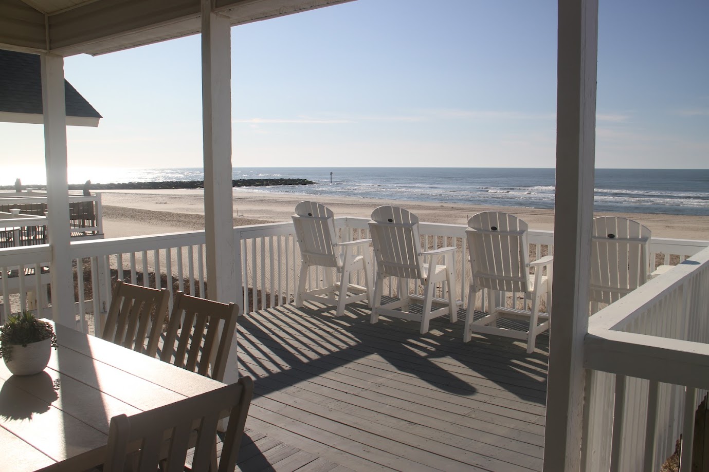 Beachfront view from a porch with wooden chairs and a dining table.