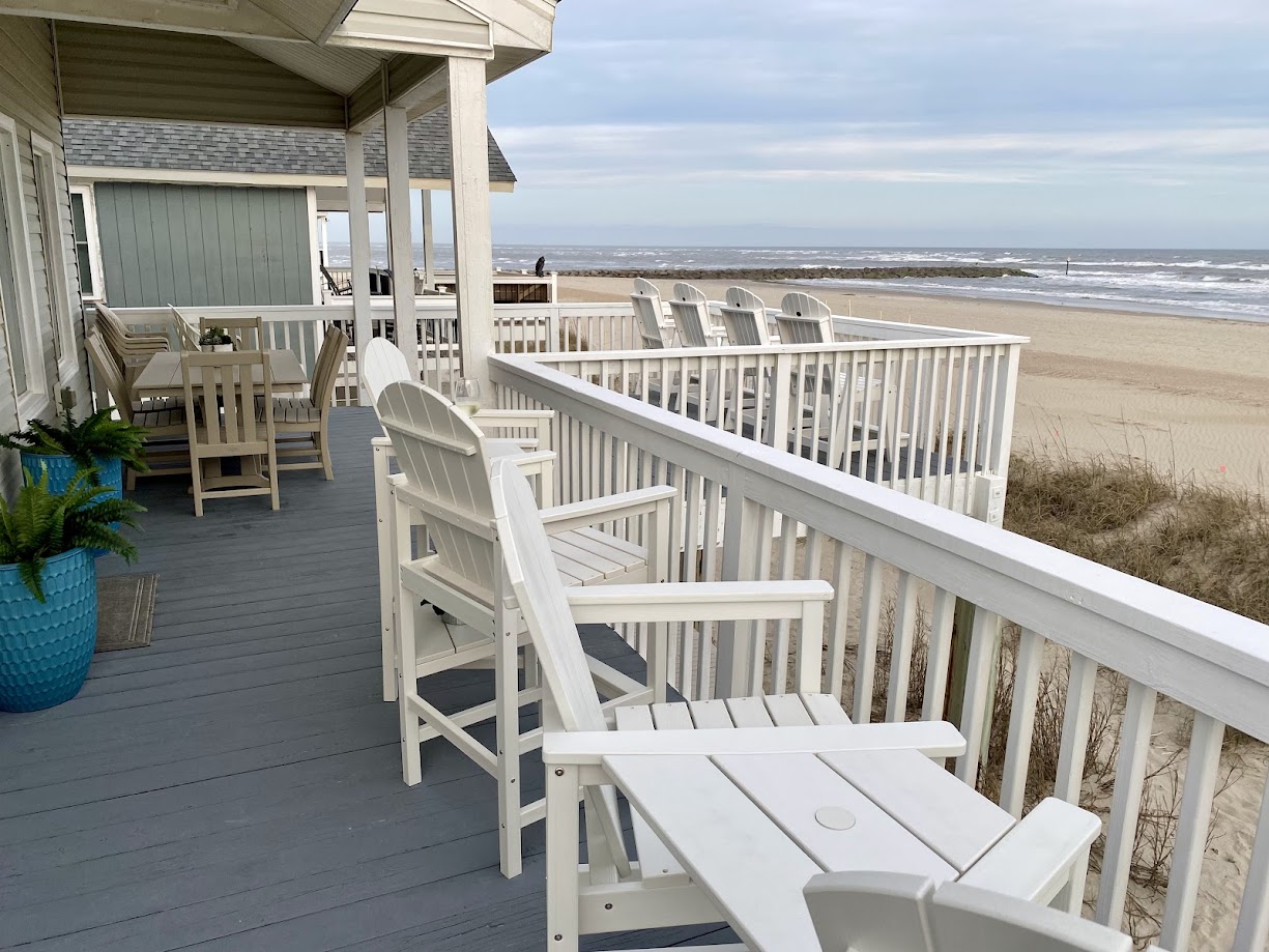 Coastal deck with white chairs and a table under a covered patio